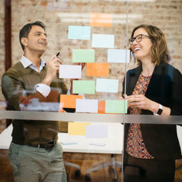Two people placing sticky notes on wall