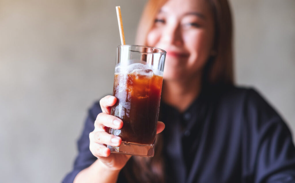 A woman holding a tall glass of soda & straw; Corporate training for organizations that sell consumer packaged goods.