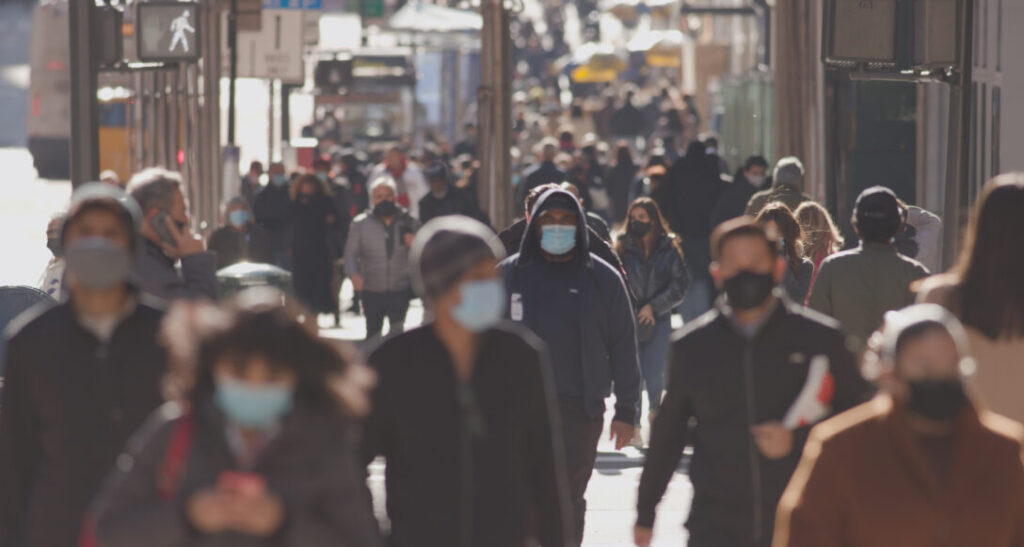 A crowd wearing medical masks walk through a city, showcasing the impact of innovation training in the healthcare industry.