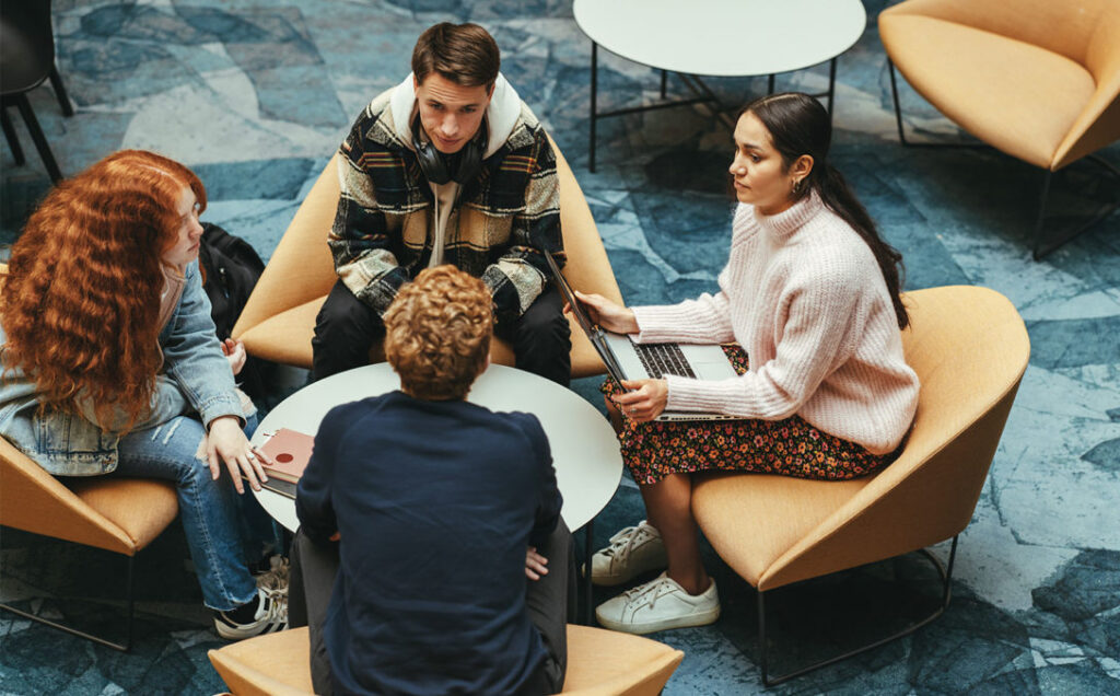 Four students chat while sitting, representing the impact of simulation-based training in executive education programs.