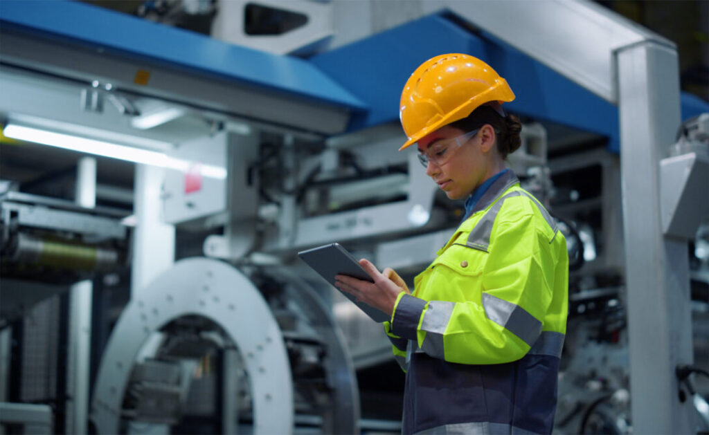 A female engineer in safety gear using a tablet, representing the impact of innovation training on the automotive industry.
