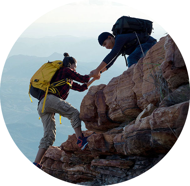 Two hikers help each other climb a mountain.